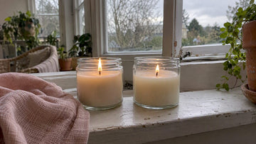 Two candles burn beside a cracked window